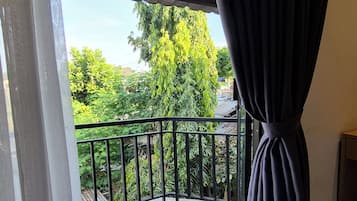 A balcony with a metal railing, a view of greenery, and a dark curtain.