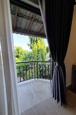 A balcony with a metal railing, a view of greenery, and a dark curtain.