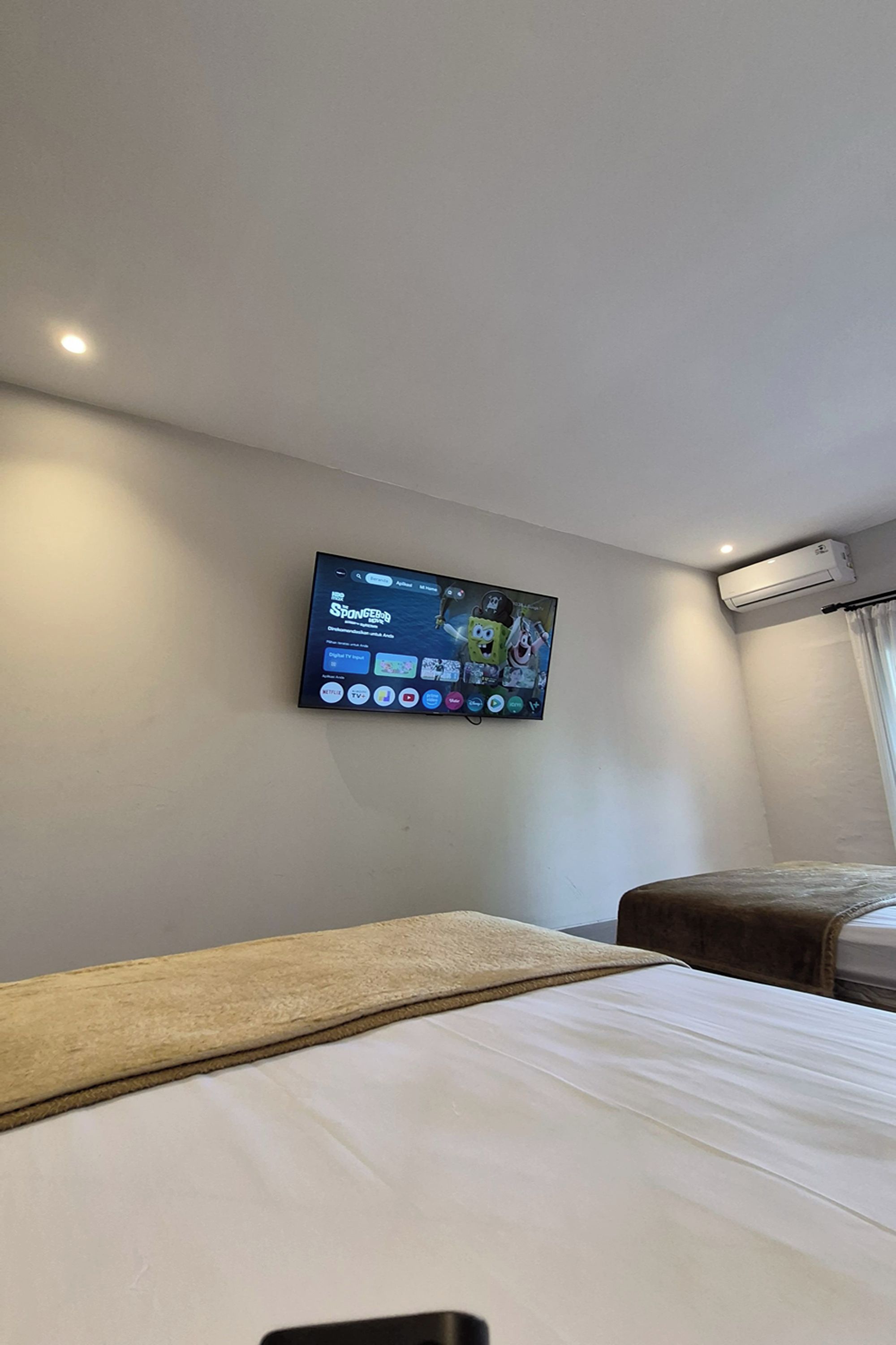 Une chambre d’hôtel avec un lit, un téléviseur fixé au mur diffusant un dessin animé et un appareil de climatisation.