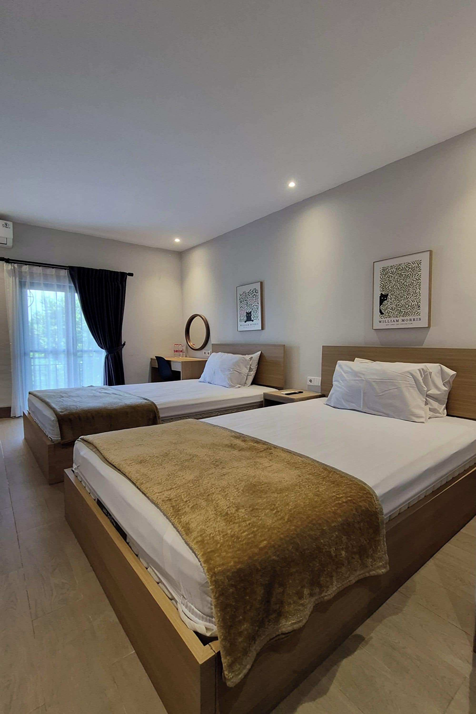 A hotel room with two beds, a desk, a chair, a mirror, and two framed pictures on the wall.