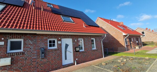 A red-tiled residential building with solar panels, numbered doors, and a brick exterior.
