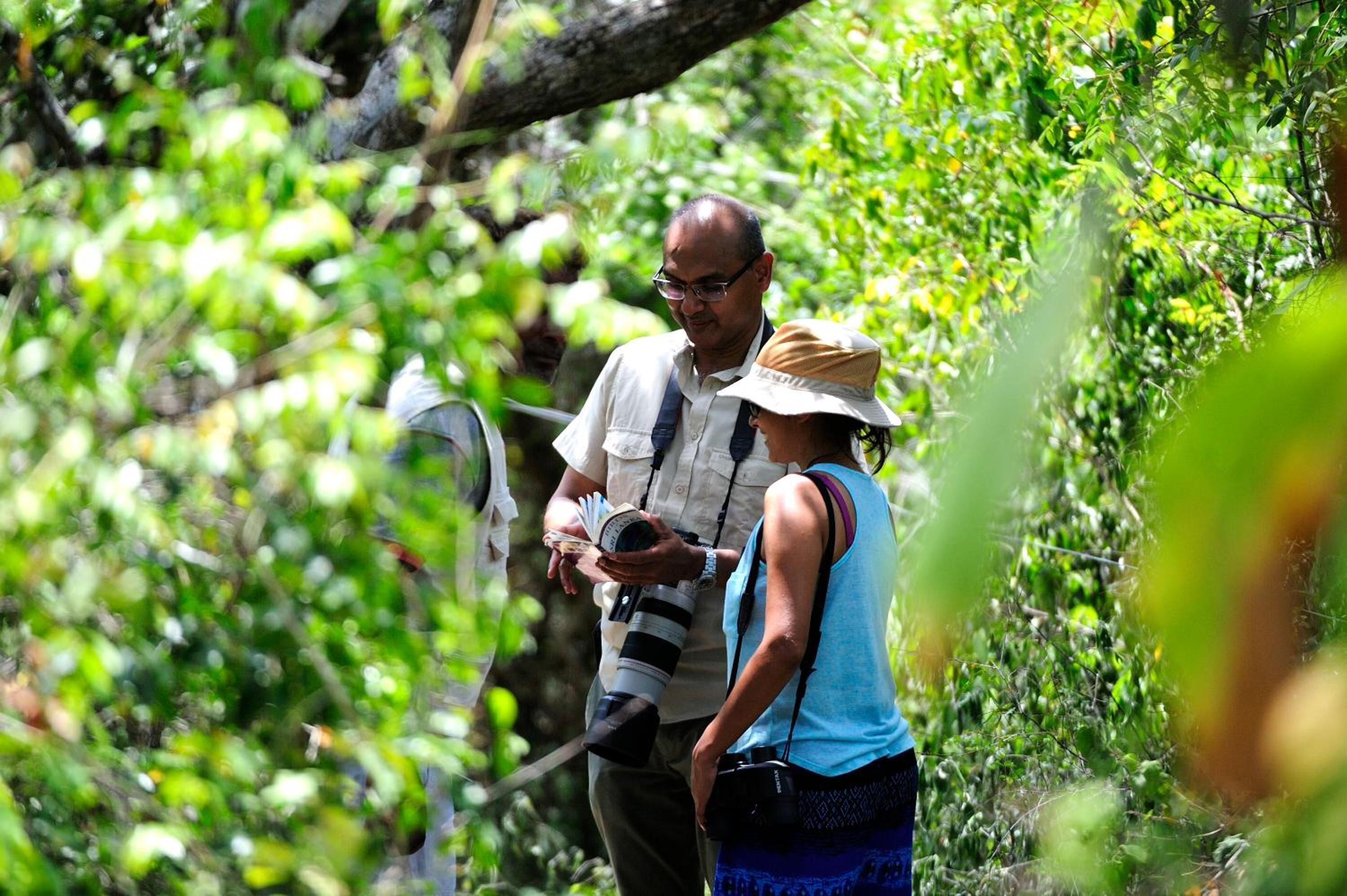 Two people in a forested area, one holding a camera.