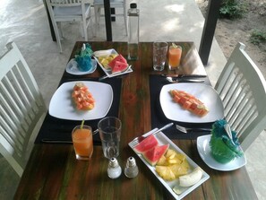Een tafel gedekt voor twee personen, met schalen watermeloen en ananas, glazen jus d'orange, en zout- en peperstel.