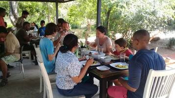 A covered outdoor dining area with people seated at tables, surrounded by greenery.
