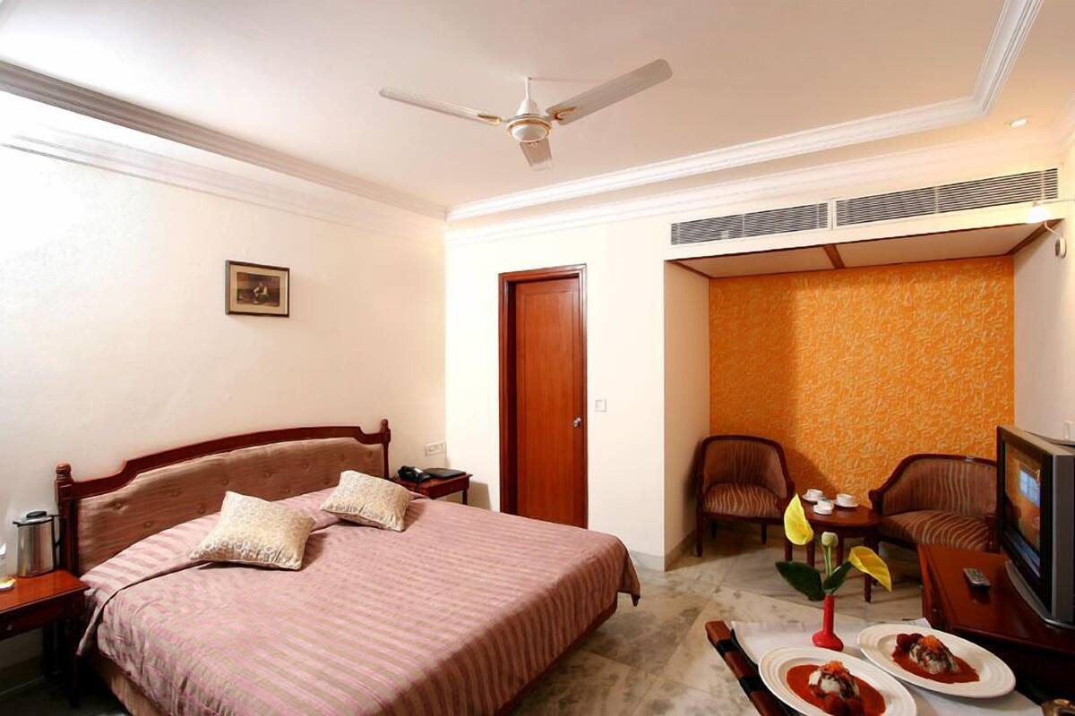 A hotel room with a bed, a TV, a dining table with plates, a chair, and a ceiling fan.