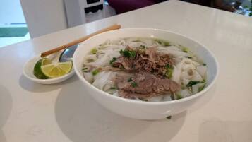 A bowl of noodle soup with beef and lime on a white table.