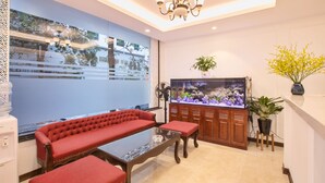 A modern living room with a red sofa, a glass coffee table, a large fish tank, and a chandelier. - Dinh Ami Hanoi Hotel (Hanoi)