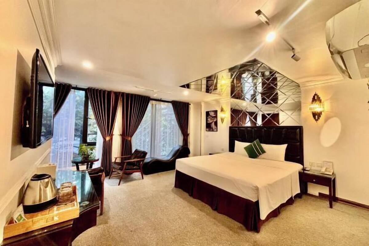 Une chambre d’hôtel avec un grand lit, un bureau avec une bouilloire, une chaise, une fenêtre avec des rideaux et un téléviseur fixé au mur.