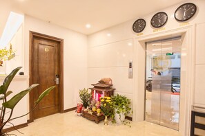 A hotel lobby with a reception desk, a wooden door with a number plaque, a traditional lantern, and clocks displaying time in Seoul, New York, and Hong Kong. - Dinh Ami Hanoi Hotel (Hanoi)