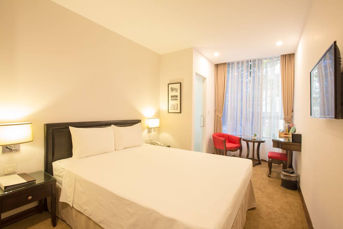 Une chambre d’hôtel avec un grand lit, une table de chevet avec une lampe, un petit bureau avec une chaise et un téléviseur fixé au mur.