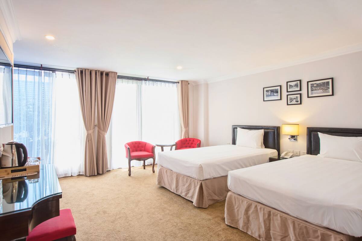Une chambre d’hôtel avec deux lits, un bureau, une chaise et une fenêtre avec des rideaux.