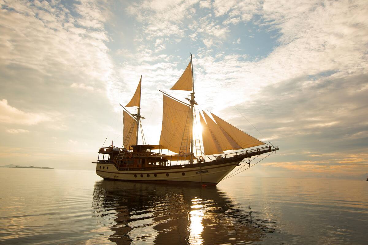 Un grand voilier à plusieurs mâts et voiles, ancré dans des eaux calmes.