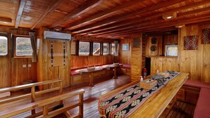 A wooden cabin interior with benches, a long table, and windows offering views of a forested landscape. - Plataran Phinisi Felicia (Labuan Bajo)