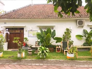 Experience the charm of Villa Sari, featuring a traditional tiled roof and a beautiful front yard with potted plants.
