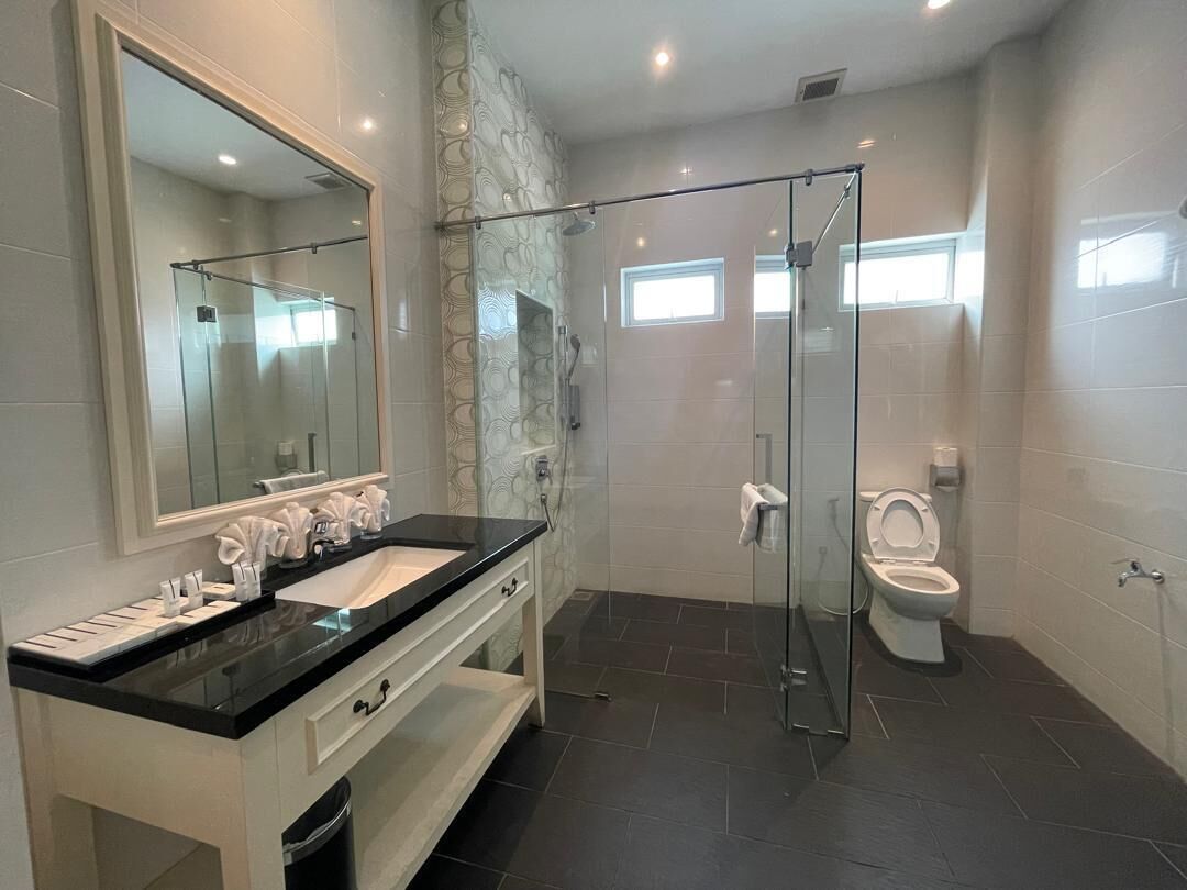 A modern bathroom with a glass-enclosed shower, a large mirror, a white sink, and a toilet.