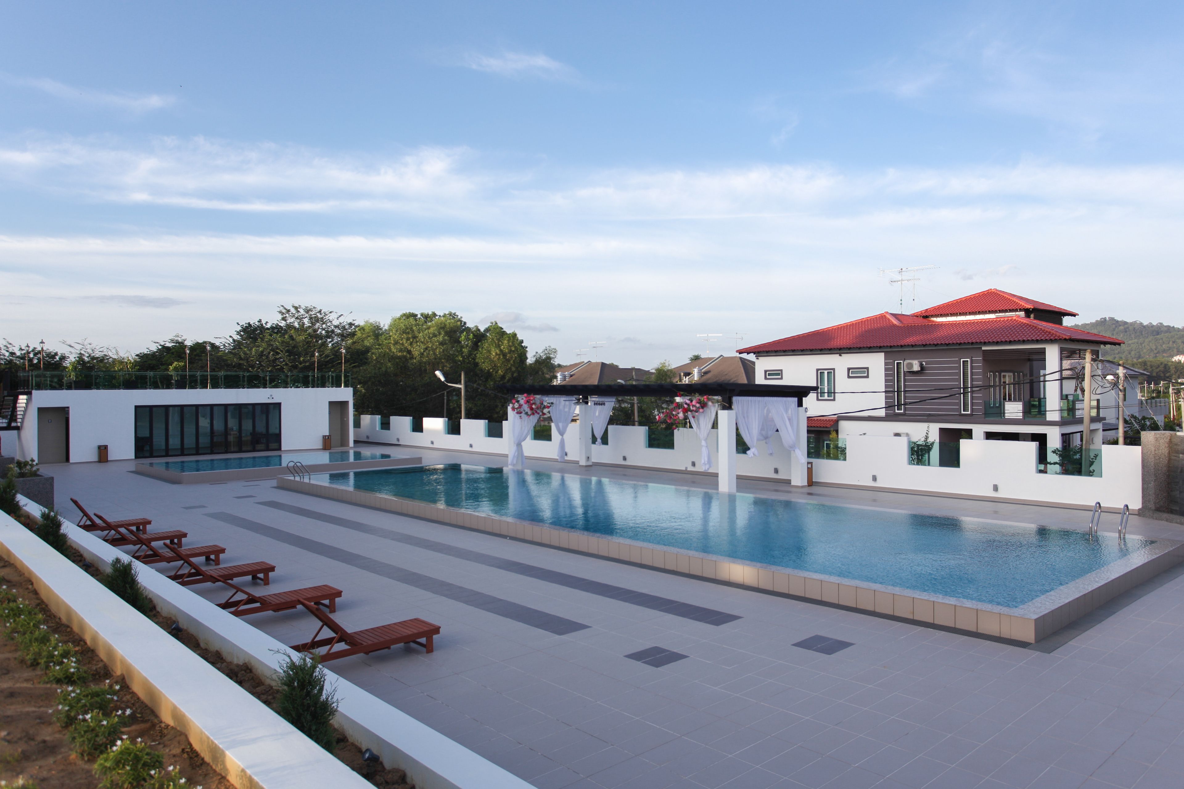A modern swimming pool area with lounge chairs and a red-roofed building.