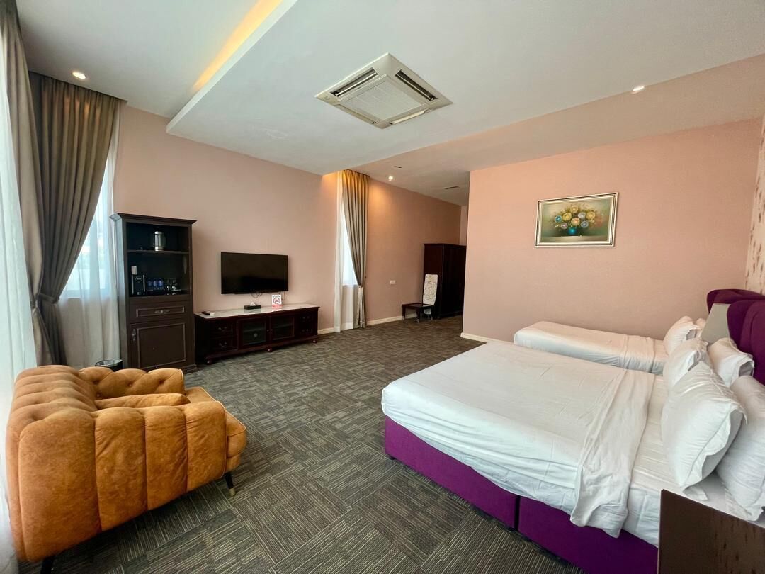 A hotel room with a large bed, a sofa, a TV, a cabinet, and a painting on the wall.