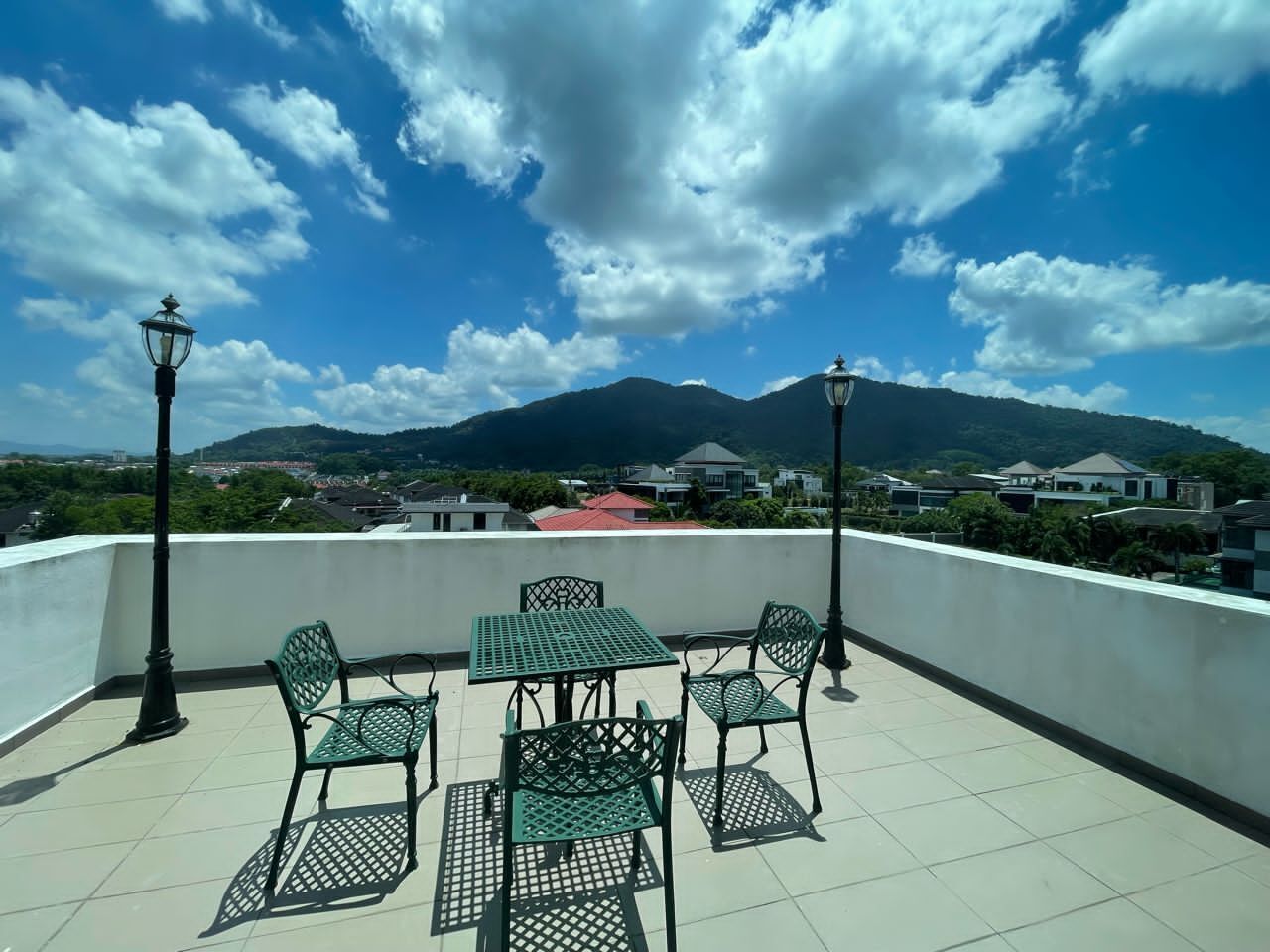 Terraza en la azotea con una mesa, sillas, dos faroles y vistas a una montaña y edificios.