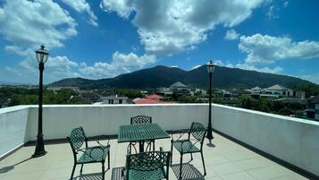 Terraza en la azotea con una mesa, sillas, dos faroles y vistas a una montaña y edificios.