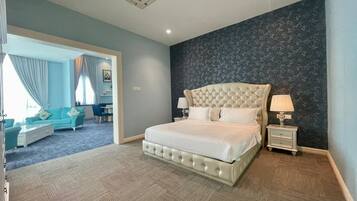Un dormitorio con una cama grande, una mesita de noche, una lámpara, un aparador y vistas a una sala de estar con un sofá y cortinas.