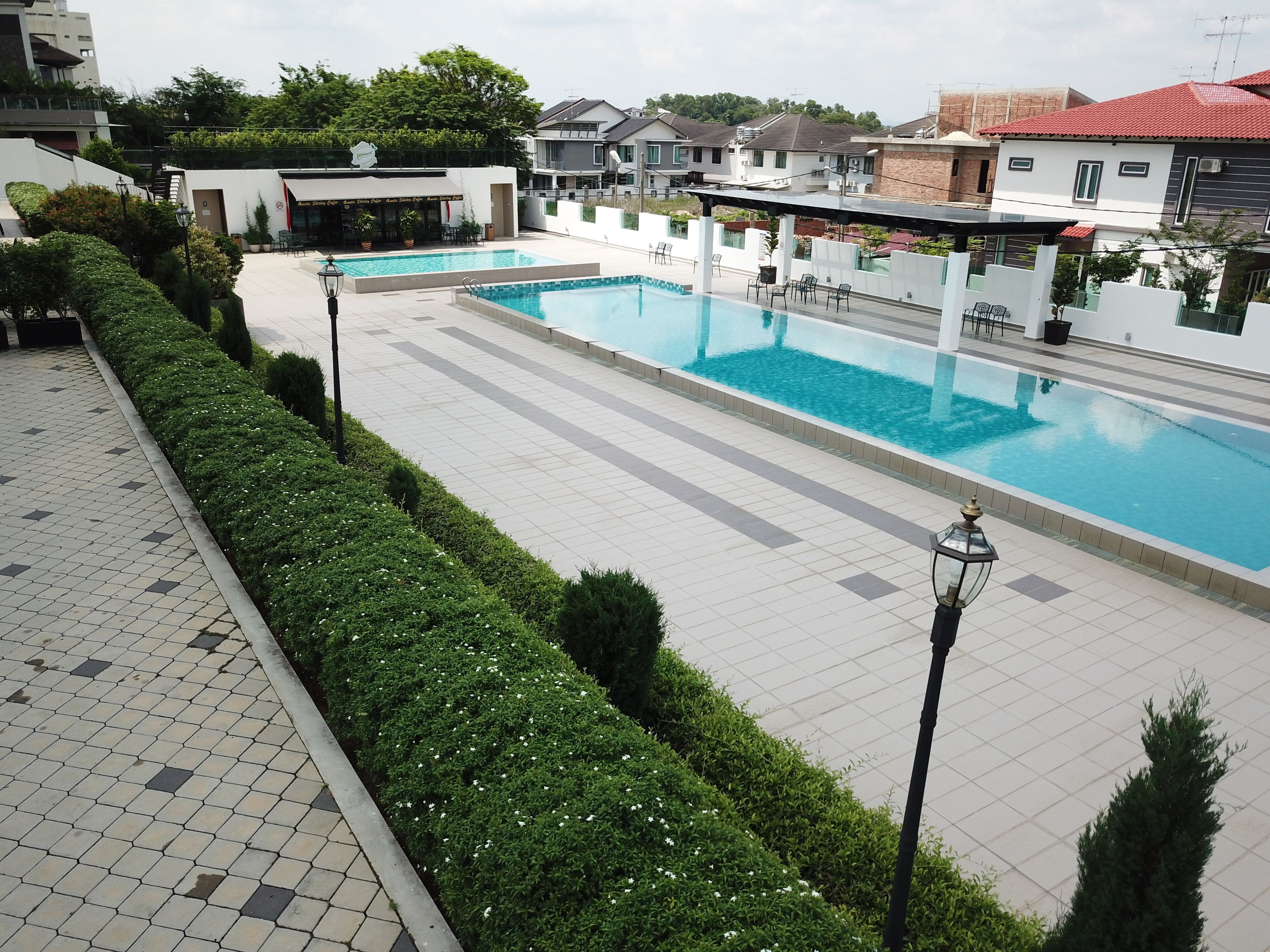 A swimming pool with tiled flooring, surrounded by neatly trimmed hedges and a few chairs.