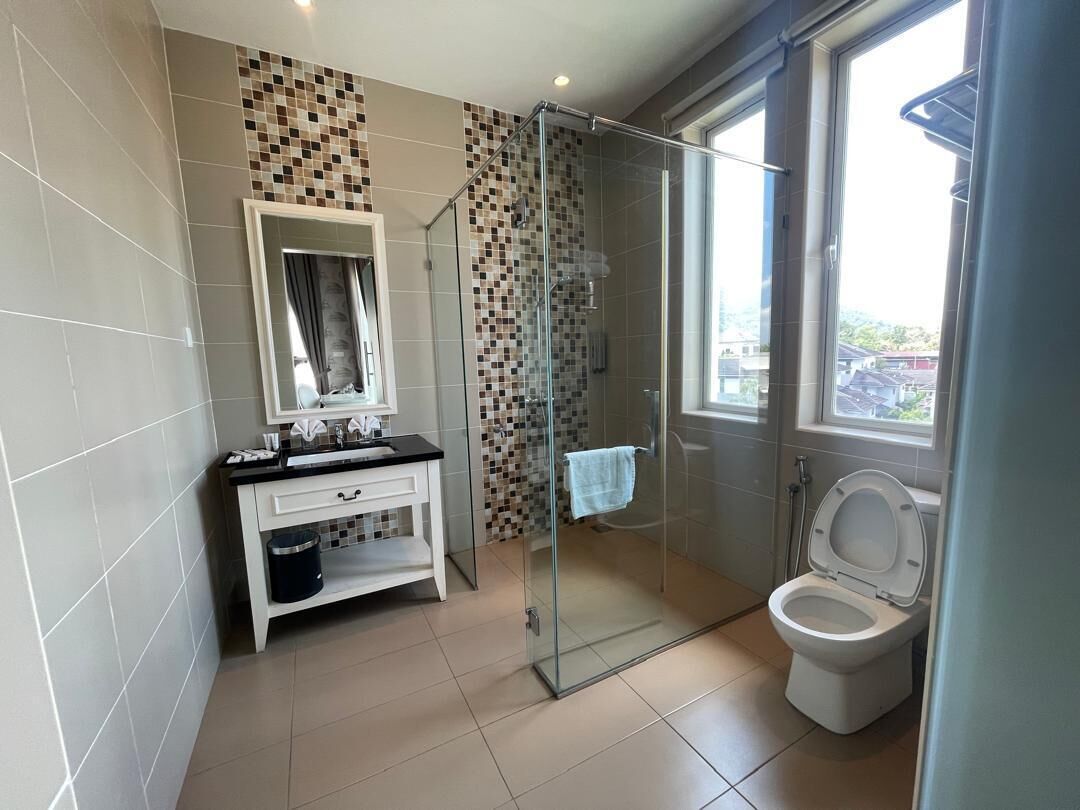 Un baño con cabina de ducha de vidrio, inodoro, lavamanos con espejo y salpicadero de azulejos.