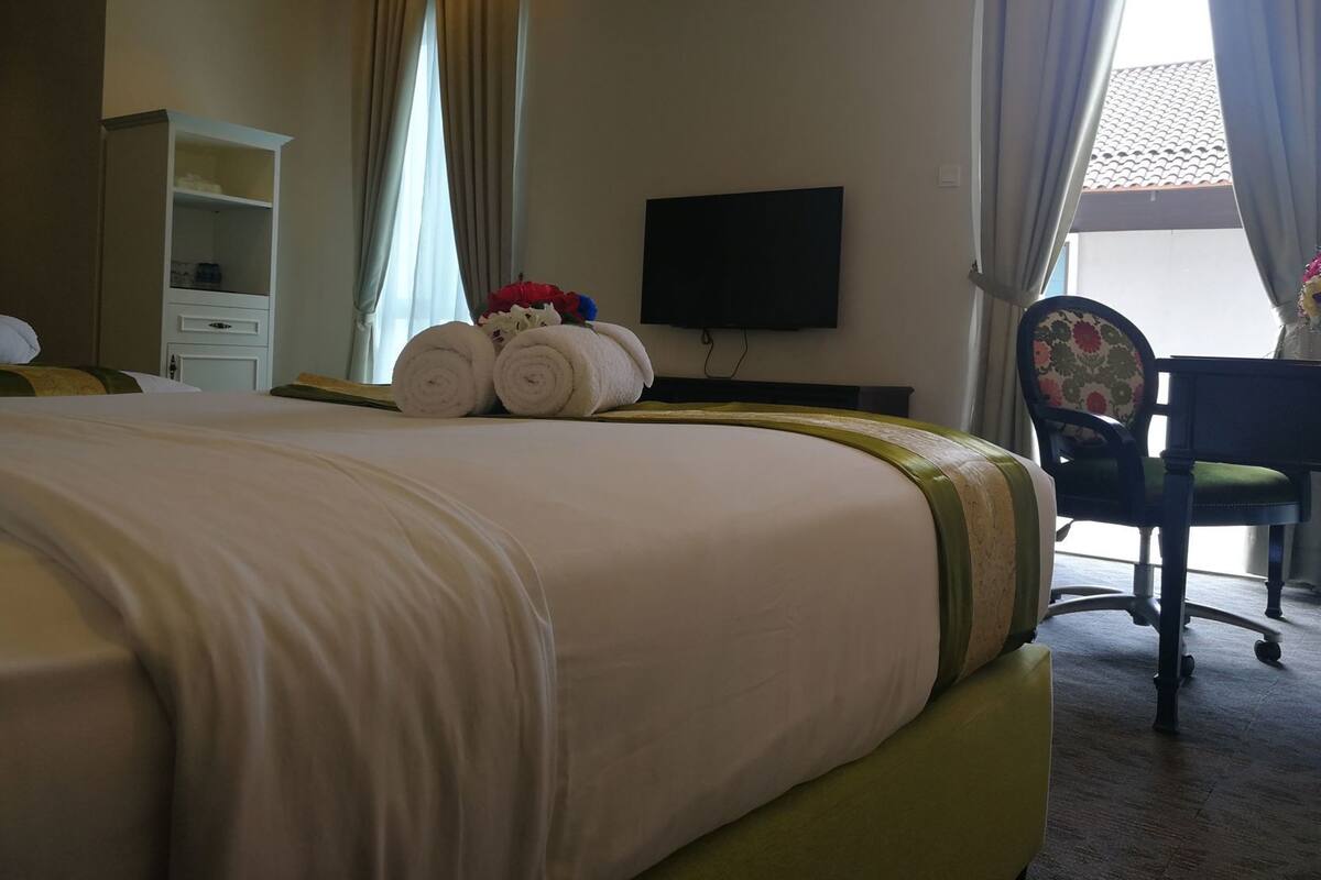 A hotel room with a large bed, a television, a desk with a chair, and a window with curtains.