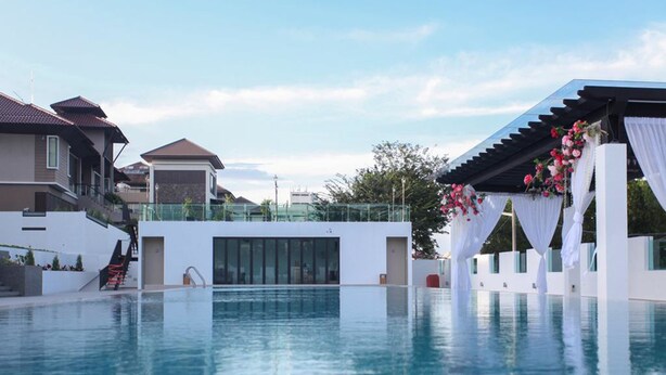 Un área de piscina moderna con vista despejada, una zona de estar techada con cortinas blancas y una escalera que lleva a un edificio residencial.
