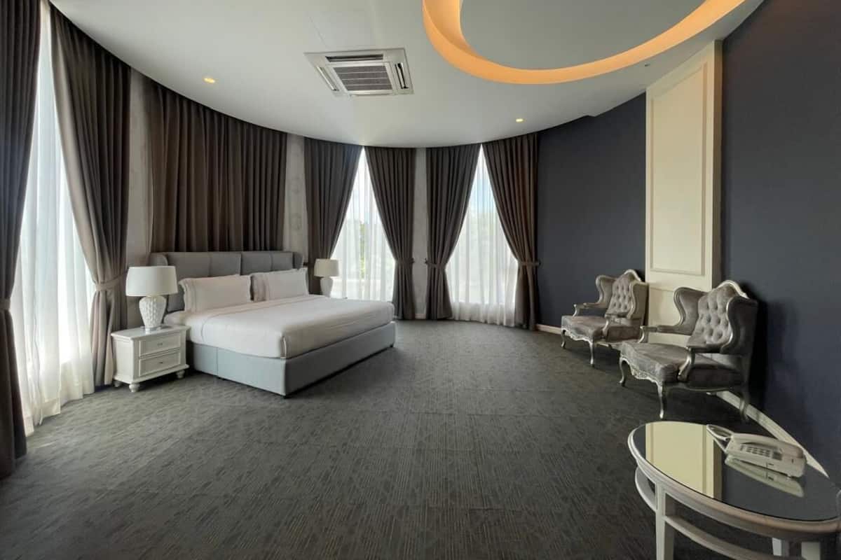 A modern hotel room with a curved ceiling, a large bed, two armchairs, a small table, and a large window.