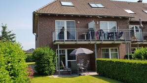 A two-story brick house with a balcony, a patio with chairs and an umbrella, and a well-maintained garden.