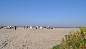 A sandy beach with beach chairs and umbrellas, a wooden fence, and a clear blue sky.