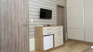 Una habitación compacta con un armario de madera, un refrigerador blanco pequeño, un televisor de pantalla plana montado en la pared y un closet con puerta corredera.
