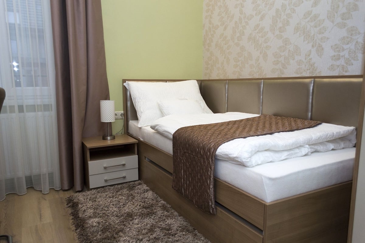 A neatly made bed with a brown blanket, a bedside lamp, and a small drawer unit.