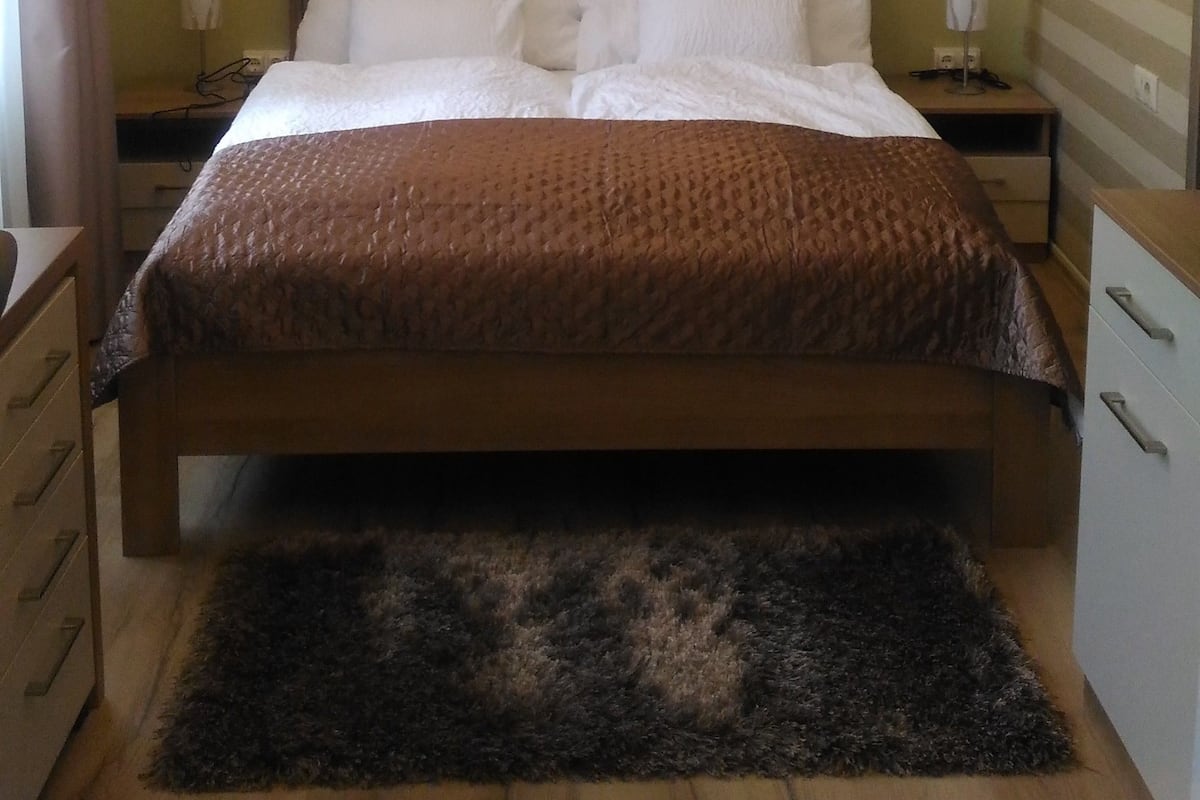 A bedroom with a bed, bedside tables, a rug, and a hanging lamp.