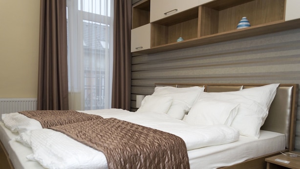 Una cama bien hecha con una manta marrón, un cabecero de madera y una mesita de noche con una lámpara.