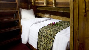 A wooden cabin room with a bed, a window, and a shelf with bottles. - Plataran Phinisi Waecicu (Labuan Bajo)
