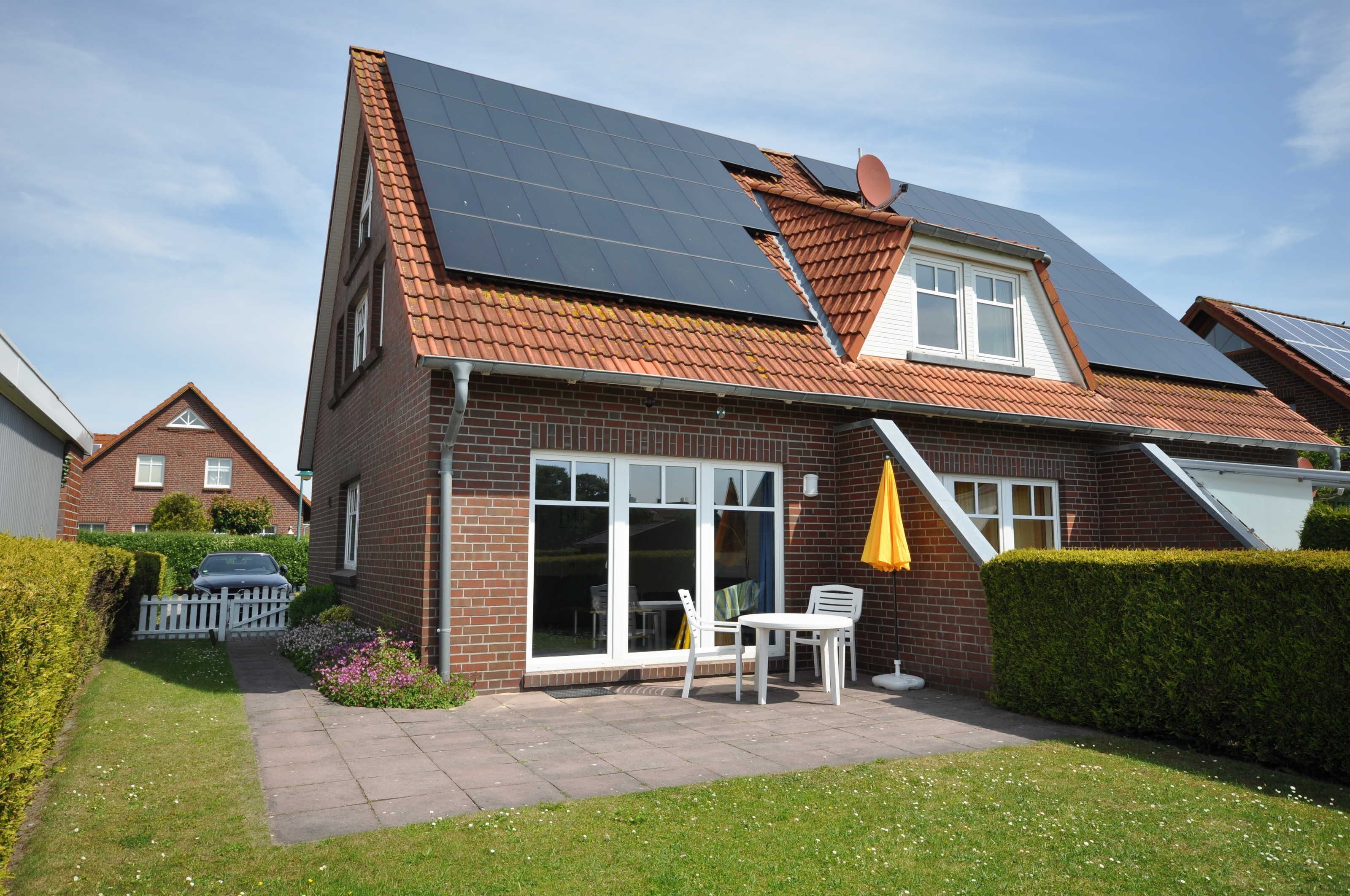 A house with a sloped roof, solar panels, a large sliding glass door, and a patio with outdoor furniture.