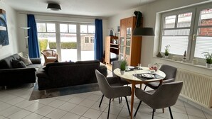Ett modernt vardagsrum med en soffa, ett matbord, stolar och en bokhylla.