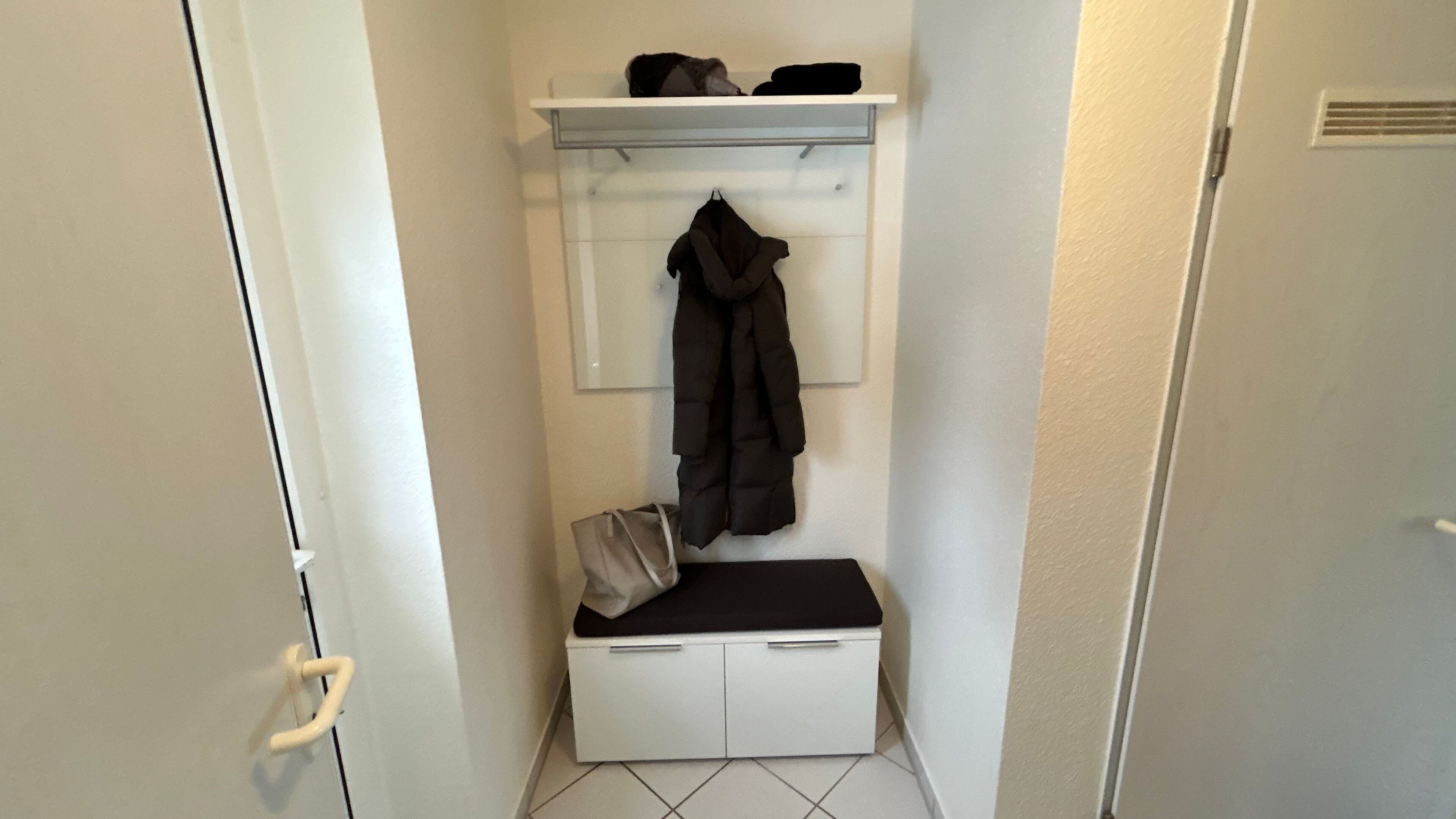 Un petit couloir étroit, avec un porte-manteau, un banc et une porte.