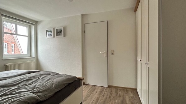 A bedroom with a bed, a wardrobe, a door, and a window.