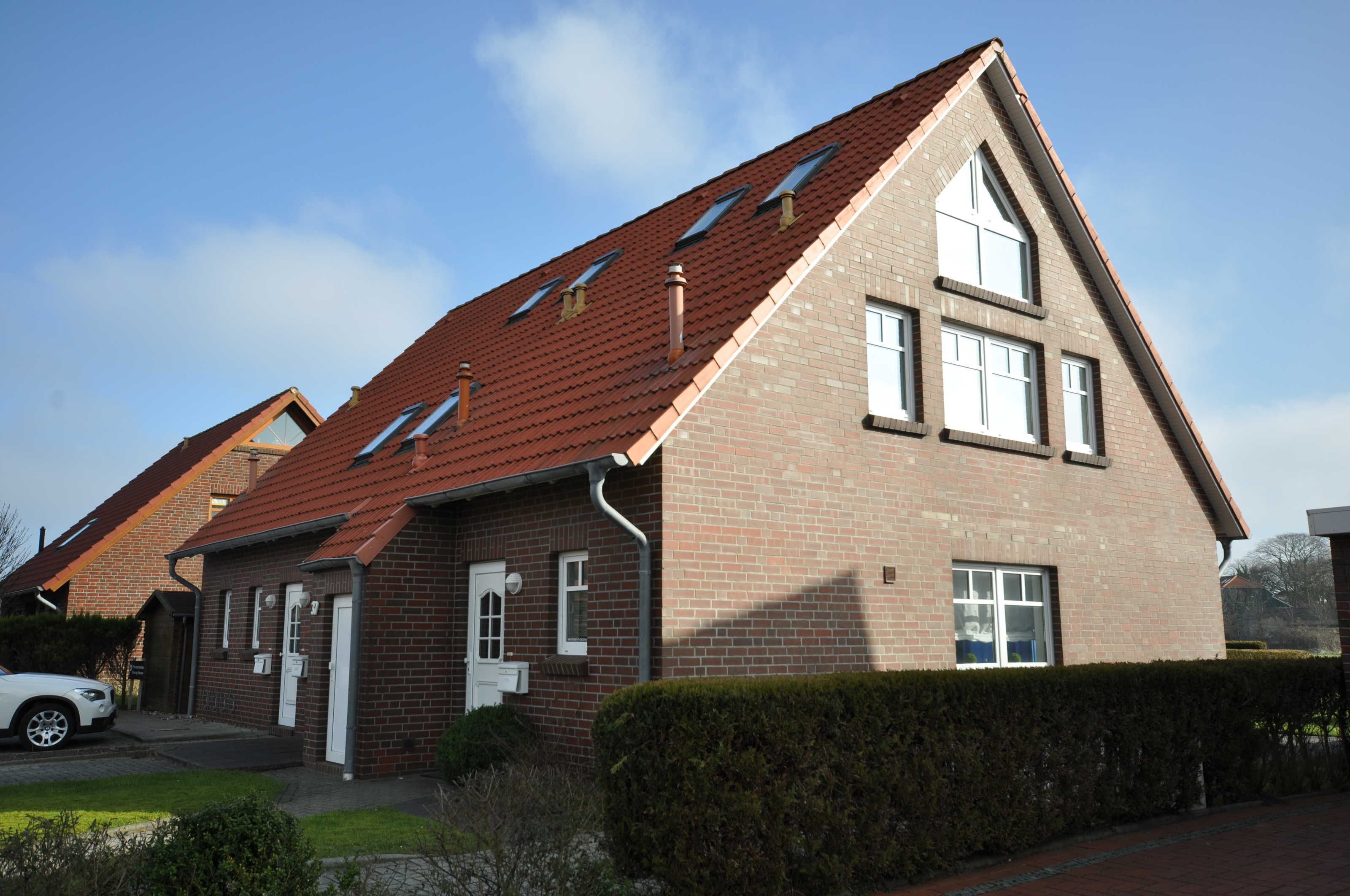 Ein zweistöckiges Backsteinhaus mit geneigtem Dach, mehreren Fenstern und einer sichtbaren Garage.