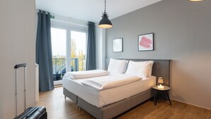 Una habitación de hotel moderna con una cama grande, una mesita de noche con lámpara y una maleta.