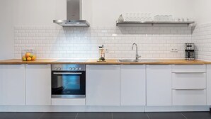 Una cocina moderna con armarios blancos, una campana extractora de acero inoxidable, un horno empotrado, un lavamanos con grifo y una cafetera sobre la encimera.