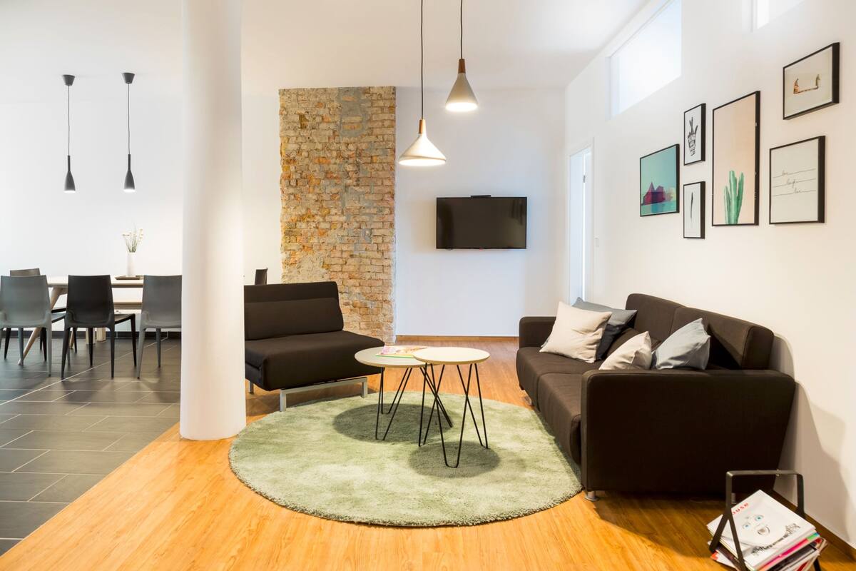 A modern living room with a brick accent wall, a flat-screen TV, and a dining area with chairs and a table.