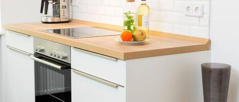 A modern kitchen with white cabinetry, a wooden countertop, an oven, and a tall vase.