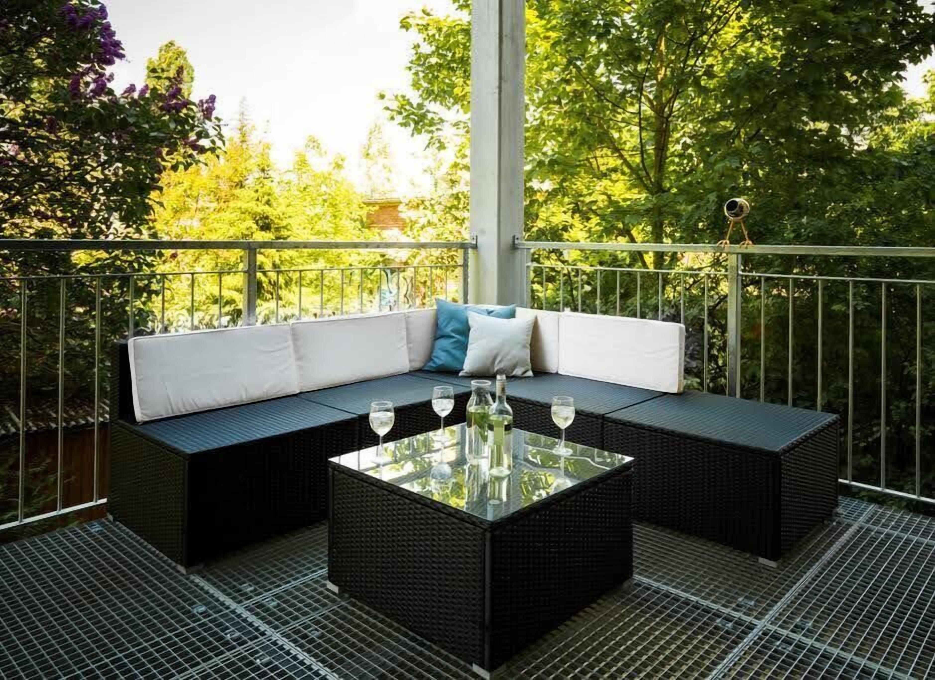 A balcony with a black wicker sofa, a glass coffee table, and a telescope.
