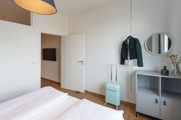 A hotel room with a bed, a suitcase, a coat hanging, a mirror, and a cabinet.