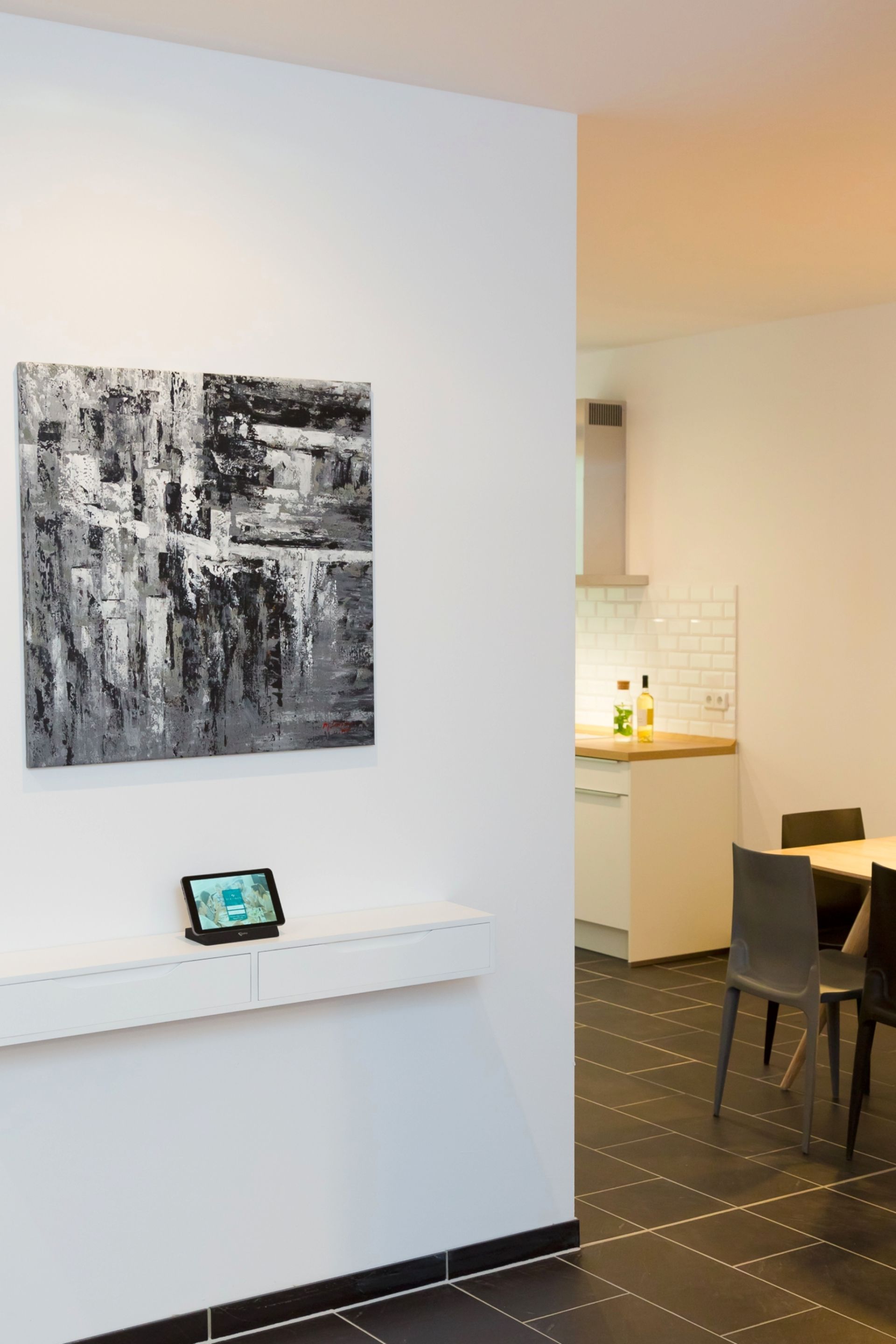 Et moderne interiør med minimalistisk design, med et stort abstrakt maleri, en tablet på en hvid konsol og et spiseområde med stole og et bord.