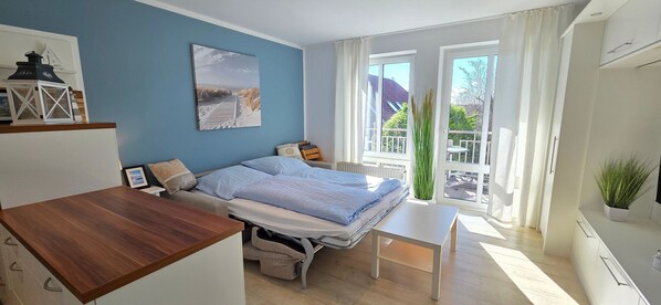A modern bedroom with a bed, a small table, and a view of the outdoors through large windows.
