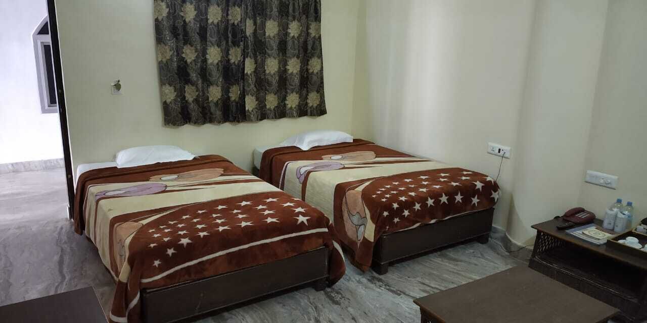 A hotel room with two beds, each with a brown blanket featuring white stars. There is a small wooden table with a phone and some items on it.